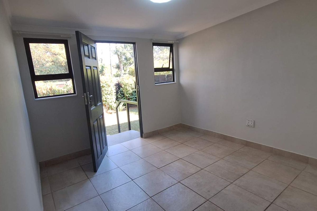 A bright, empty bedroom featuring neutral tiled flooring, aluminium window frames, and direct access to the exterior through a private door.