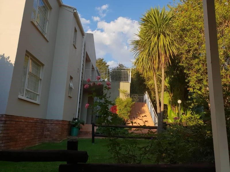 Rear view of the apartment building featuring a landscaped garden, brick exterior walls, and an external staircase with metal railings.