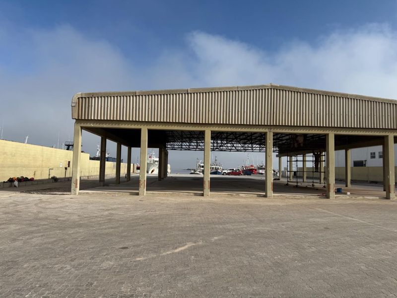 An open-sided industrial warehouse structure featuring a steel portal frame and concrete slab flooring, situated in a harbour or port environment.