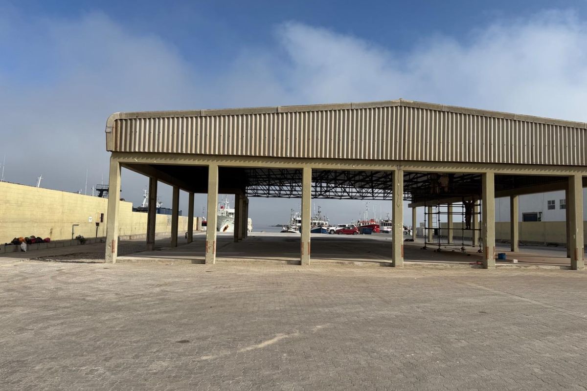 An open-sided industrial warehouse structure featuring a steel portal frame and concrete slab flooring, situated in a harbour or port environment.