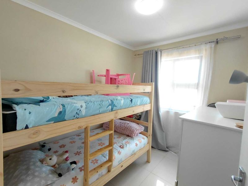 A functional bedroom featuring tiled flooring, neutral wall paint, and a window with curtain fittings, providing a bright and practical living space.