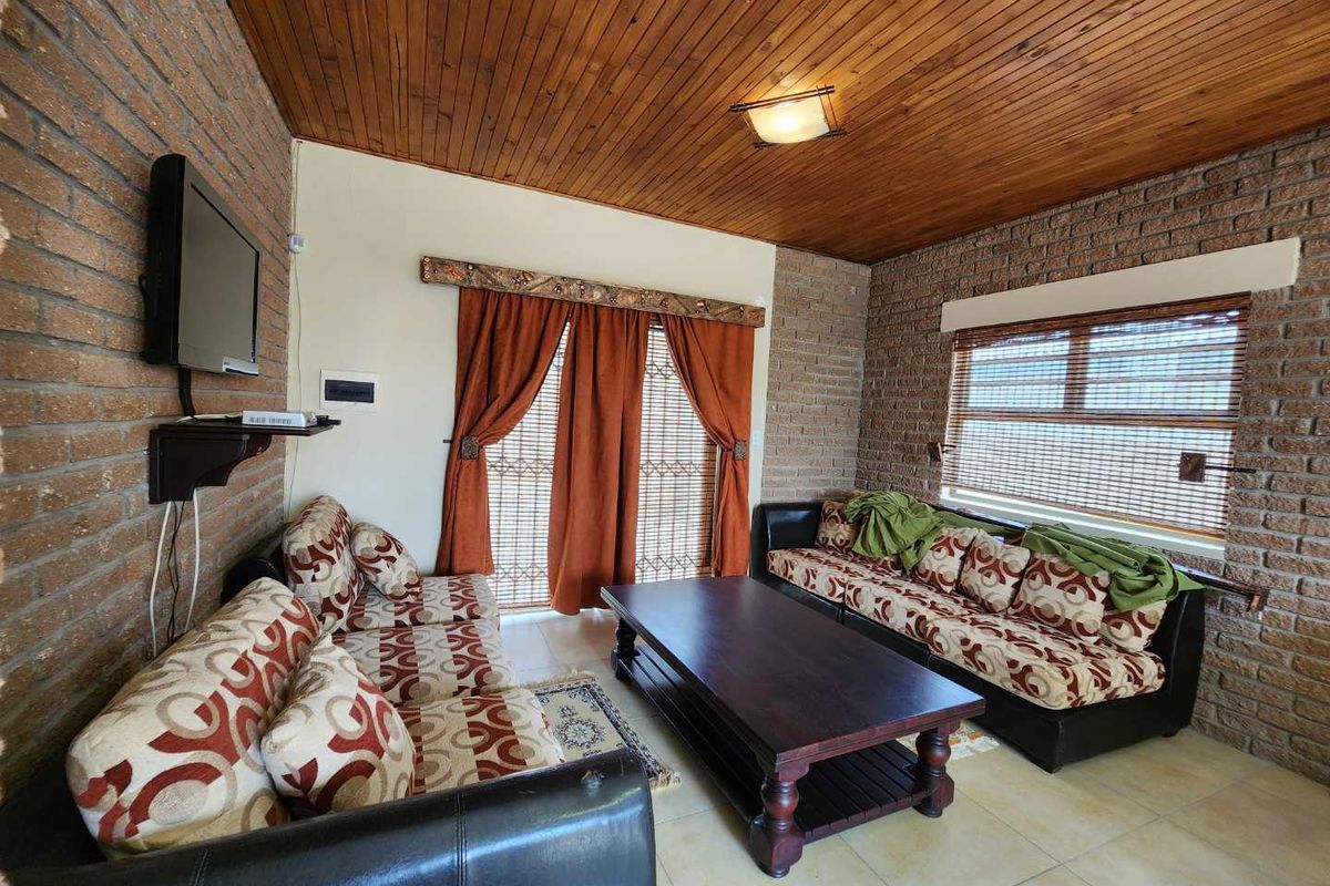 A living room featuring exposed brick walls, a timber-clad ceiling, and tiled flooring, creating a rustic aesthetic.