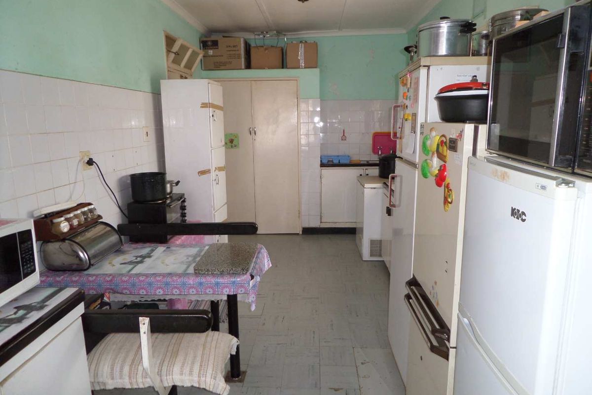 A dated kitchen featuring basic cabinetry, tiled splashbacks, and vinyl flooring, offering a functional layout with potential for modernization and renovation.