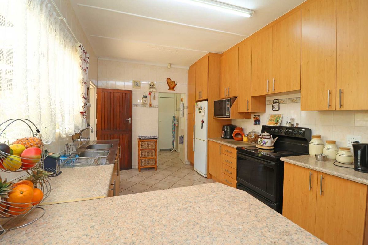 A functional kitchen featuring wood-look laminate cabinetry, laminate countertops, a double basin sink, and tiled flooring with a classic layout.