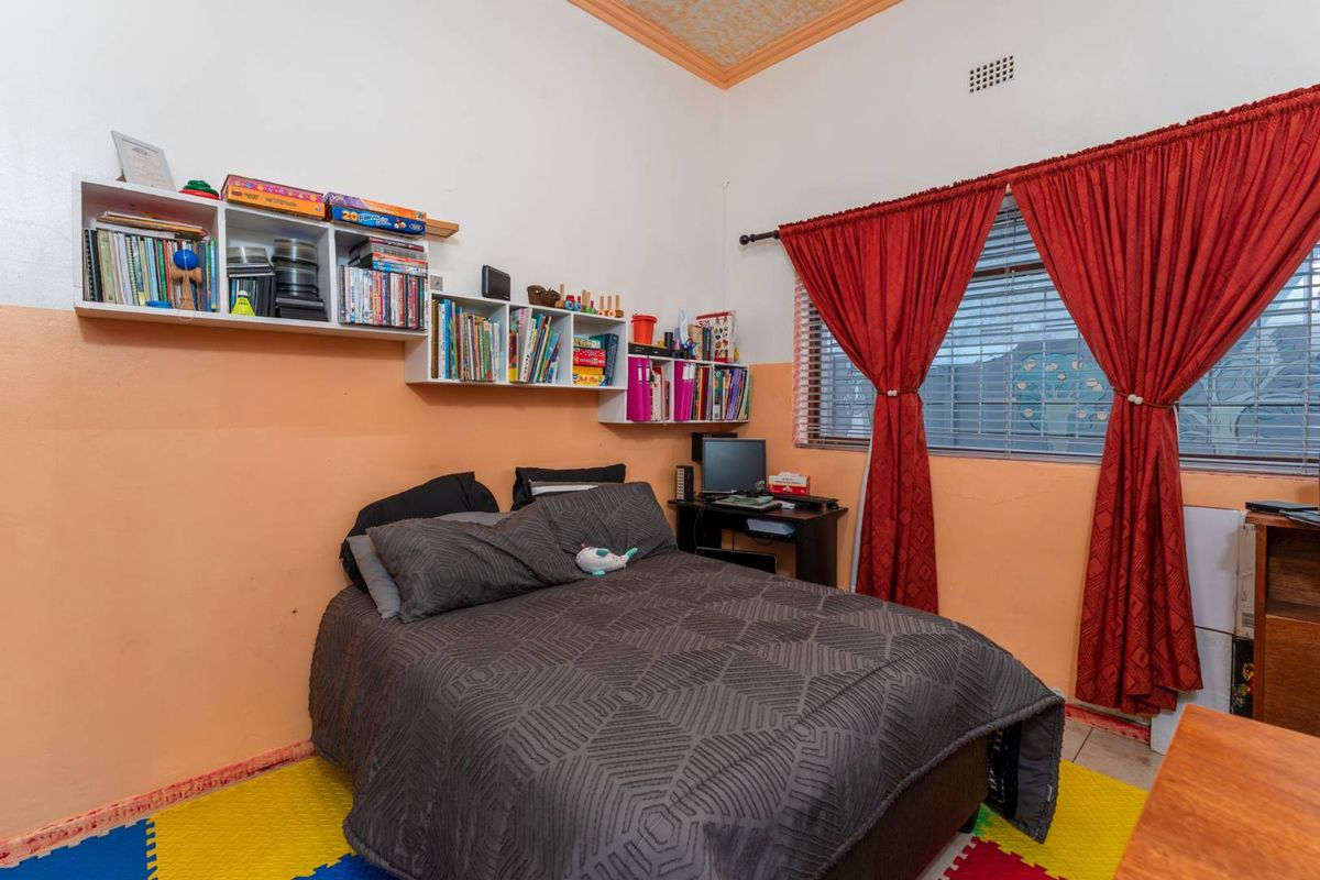 A bedroom featuring a window with red curtains, built-in wall shelving, and tiled flooring.