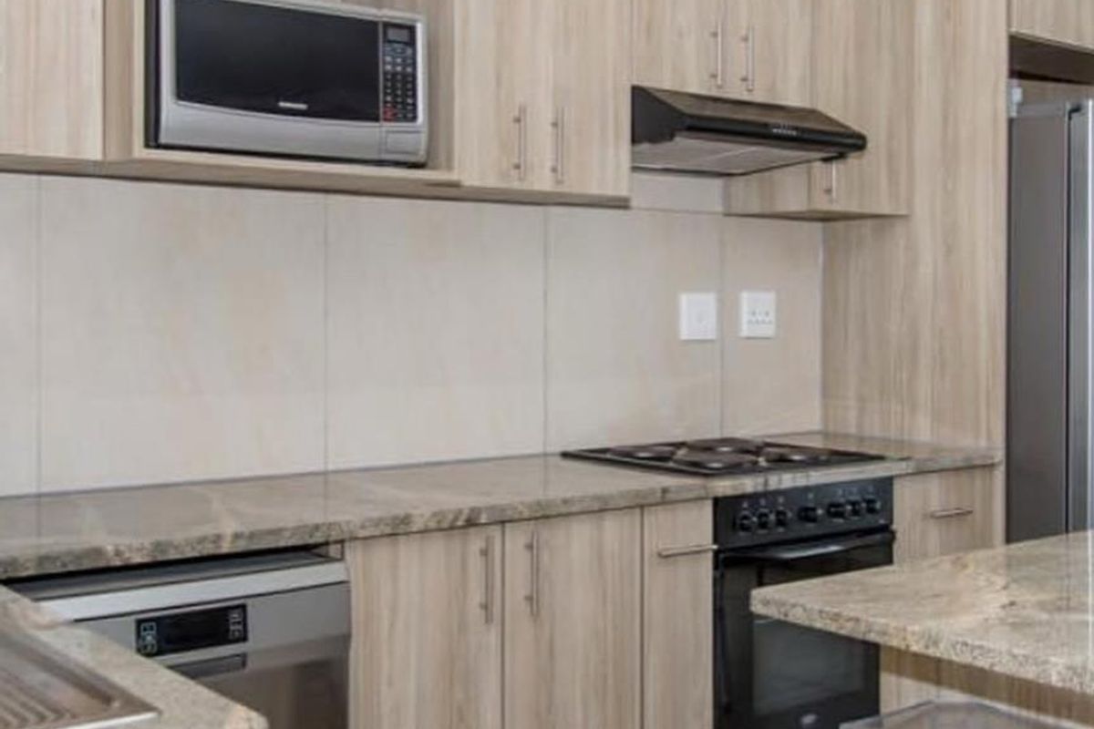 Modern kitchen featuring light wood-grain cabinetry, stone countertops, built-in oven with gas hob, extractor fan, and integrated microwave.