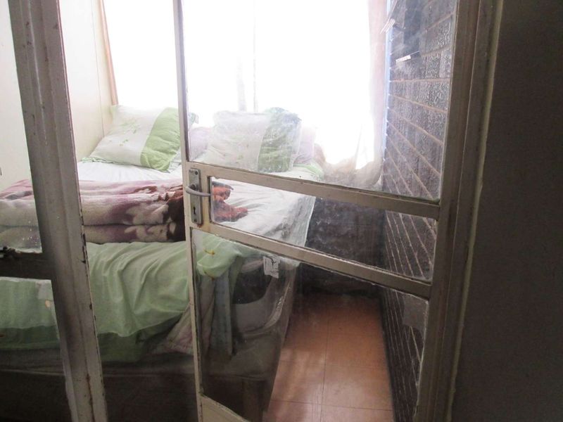 A compact bedroom featuring an exposed brick wall, tiled flooring, and a sliding glass door entrance with visible signs of wear.