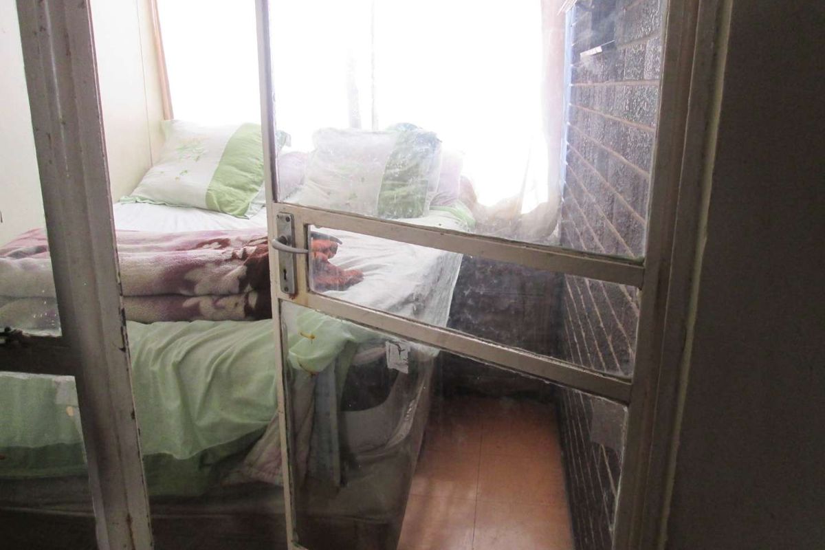 A compact bedroom featuring an exposed brick wall, tiled flooring, and a sliding glass door entrance with visible signs of wear.