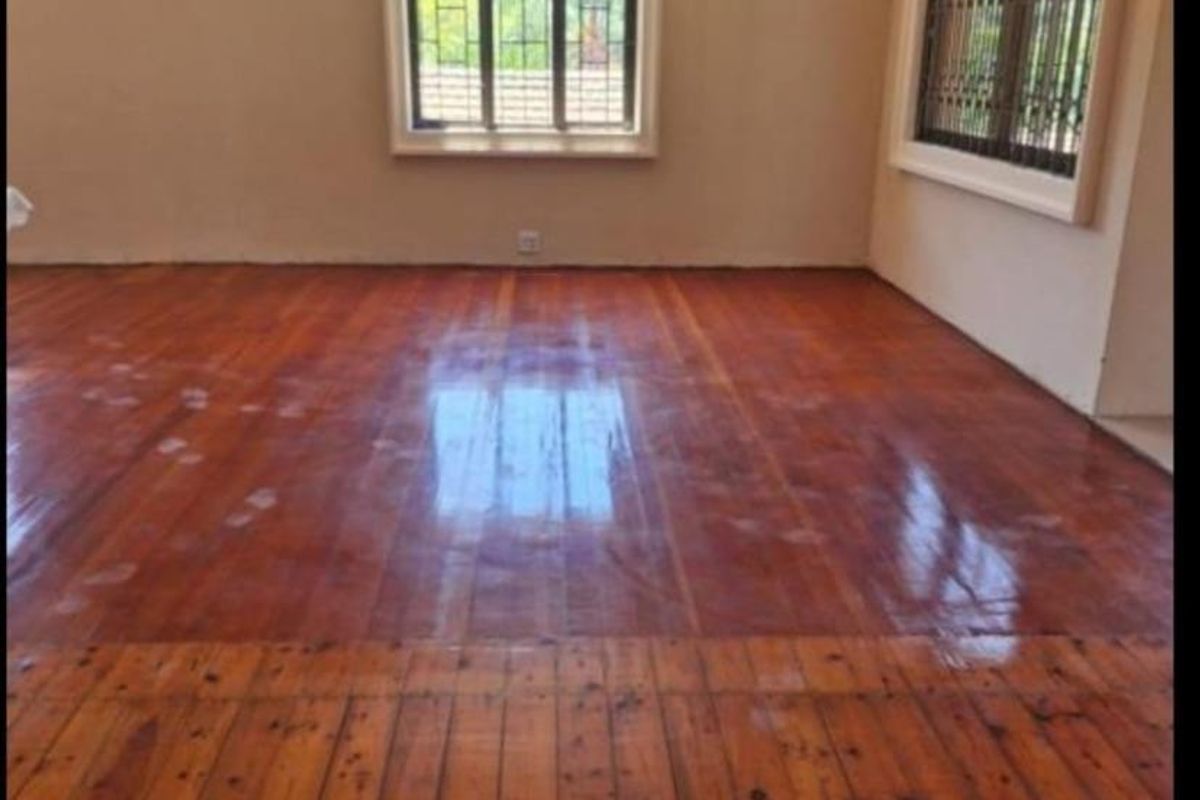An empty living room featuring polished hardwood flooring, decorative cornice detailing, and windows fitted with security bars.
