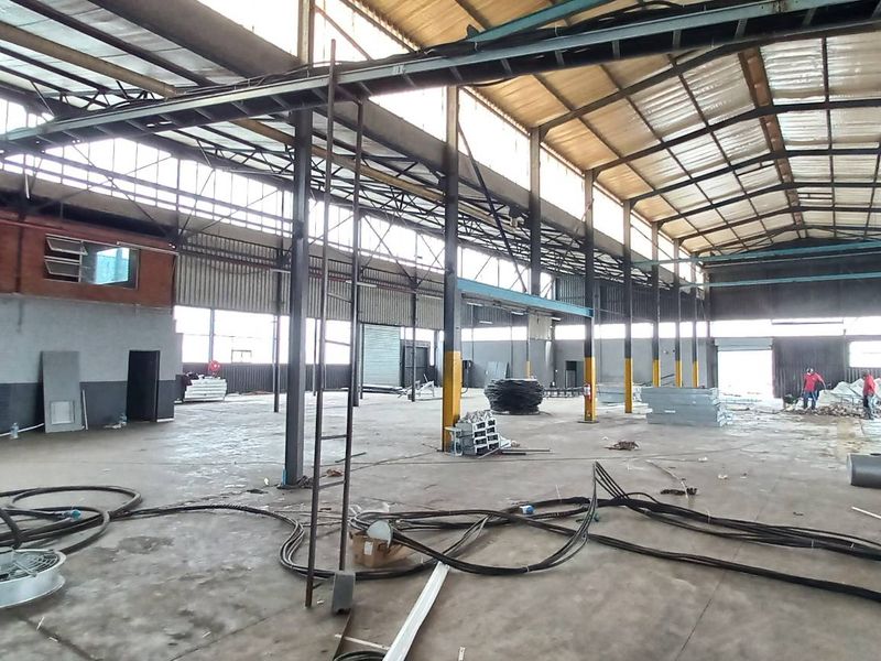 Expansive industrial warehouse space featuring high ceilings, exposed steel portal frame construction, concrete flooring, and abundant natural light from clerestory windows.