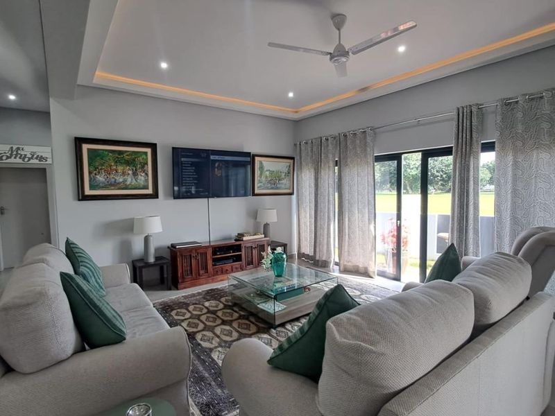 A well-maintained living room featuring a recessed ceiling with cove lighting, a ceiling fan, and large sliding glass doors providing natural light.