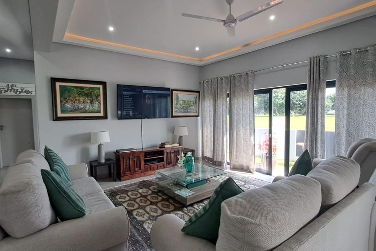 A well-maintained living room featuring a recessed ceiling with cove lighting, a ceiling fan, and large sliding glass doors providing natural light.