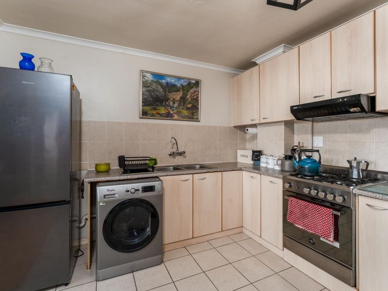 Functional kitchen featuring light wood-finish cabinetry, tiled backsplash, gas stove with extractor fan, and integrated space for a washing machine.