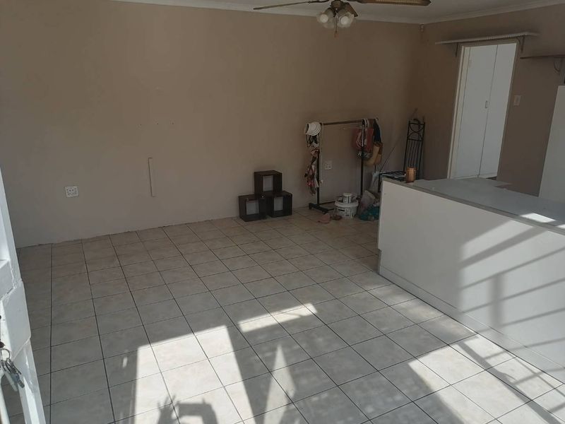 An open-plan living area featuring tiled flooring, a ceiling fan, and a built-in counter, offering a blank canvas for renovation and interior design.