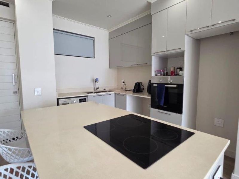 Modern kitchen featuring a central island with an integrated electric hob, built-in oven, sleek cabinetry, and stone countertops.