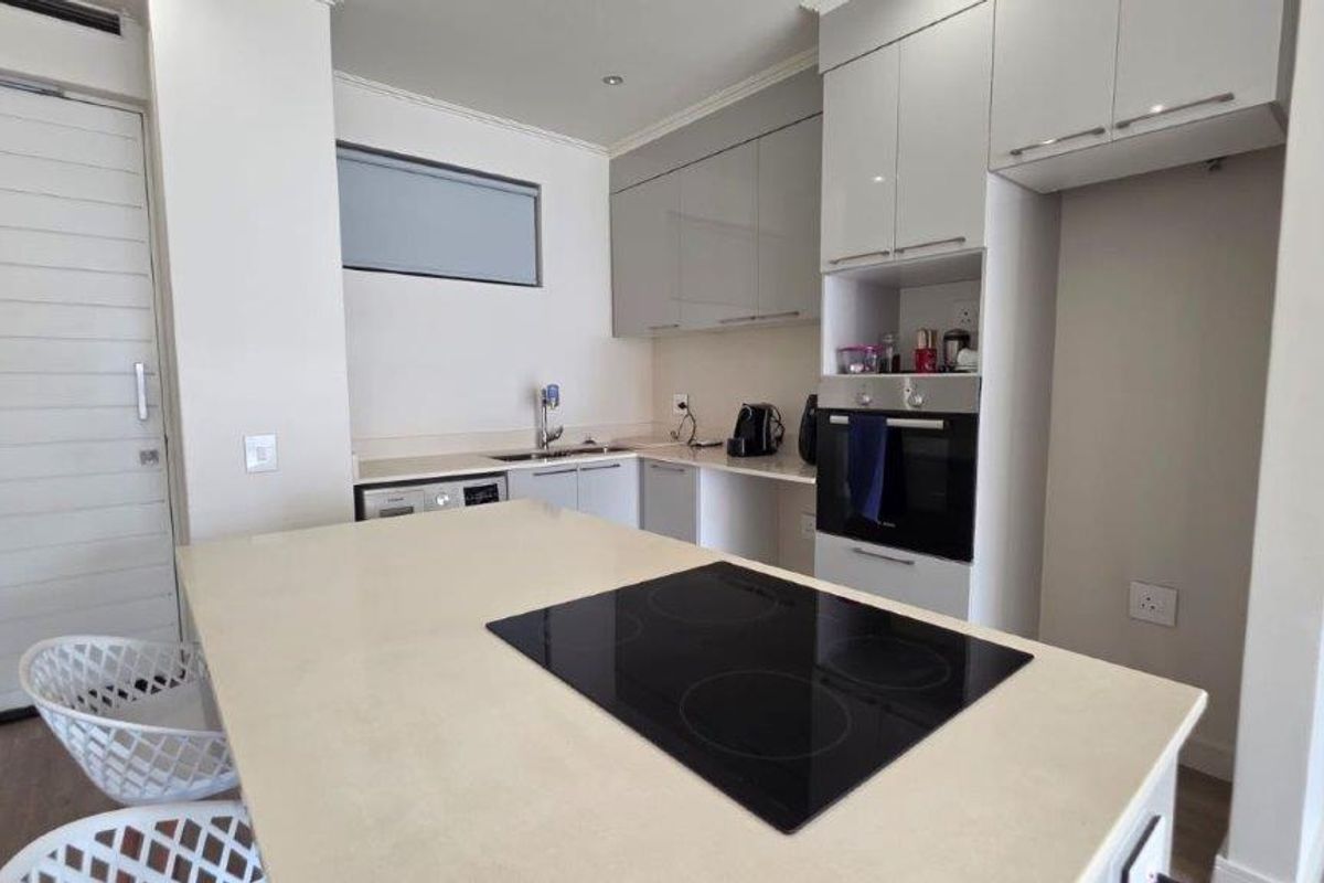Modern kitchen featuring a central island with an integrated electric hob, built-in oven, sleek cabinetry, and stone countertops.