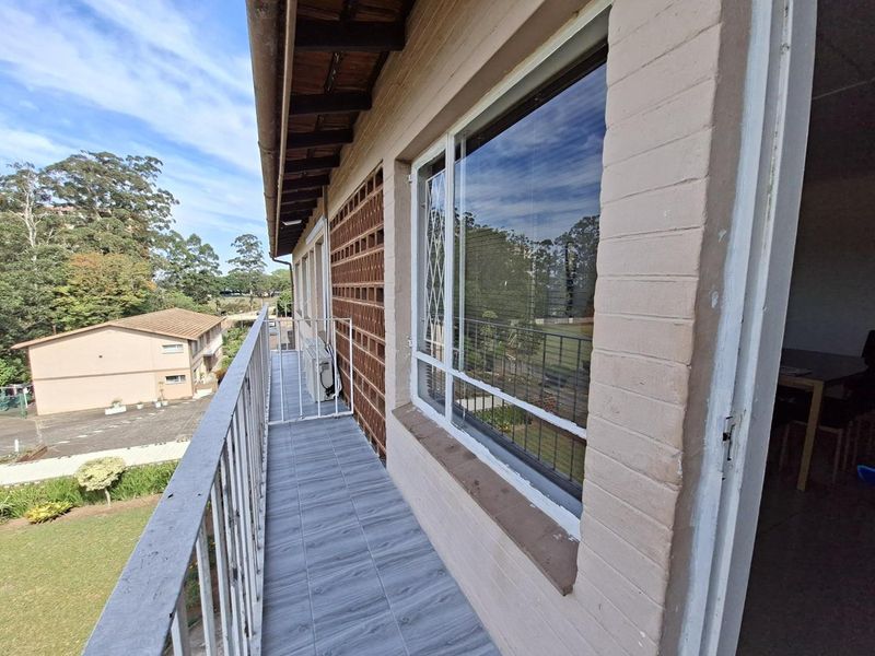 A balcony featuring tiled flooring, a metal balustrade, and a brick facade, overlooking the apartment complex grounds.