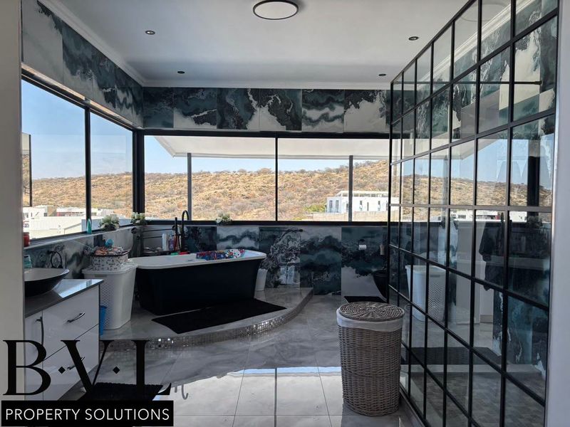 Modern bathroom featuring a freestanding bathtub, large windows with scenic views, and a stylish black metal-framed glass shower enclosure.