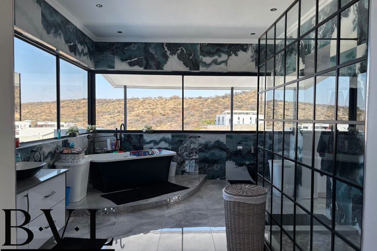 Modern bathroom featuring a freestanding bathtub, large windows with scenic views, and a stylish black metal-framed glass shower enclosure.