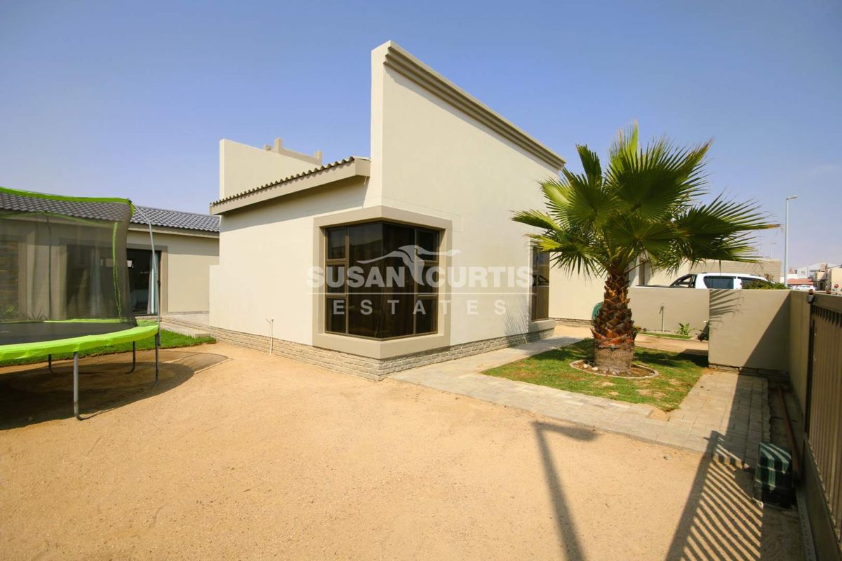 Rear view of the property featuring a modern corner window, paved walkway, and landscaped garden area with boundary wall.