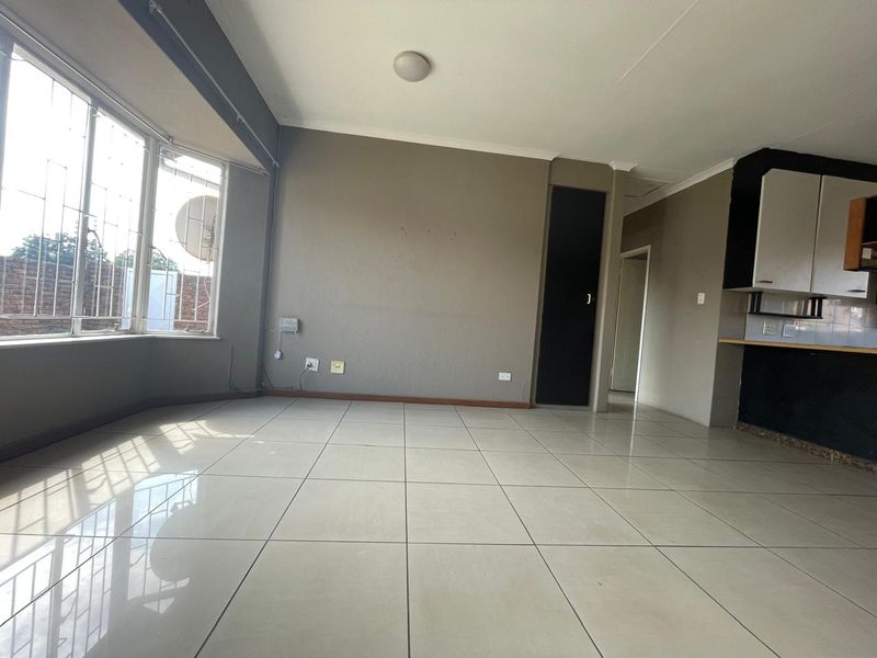 An open-plan living and kitchen area featuring tiled flooring, large windows with security bars, and built-in kitchen cabinetry.