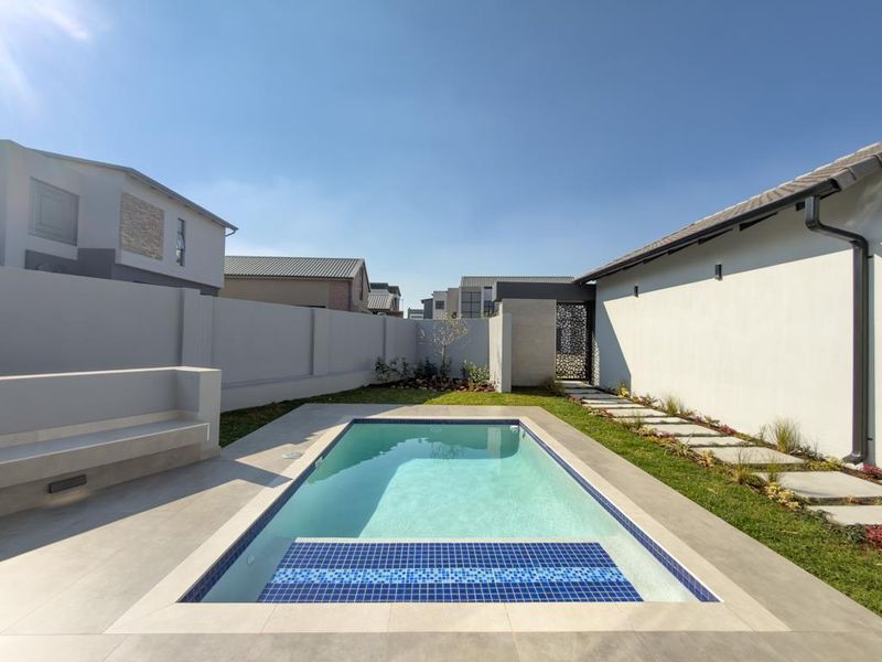 Modern outdoor pool area featuring a tiled swimming pool, built-in concrete bench seating, and a landscaped garden with a paved walkway.