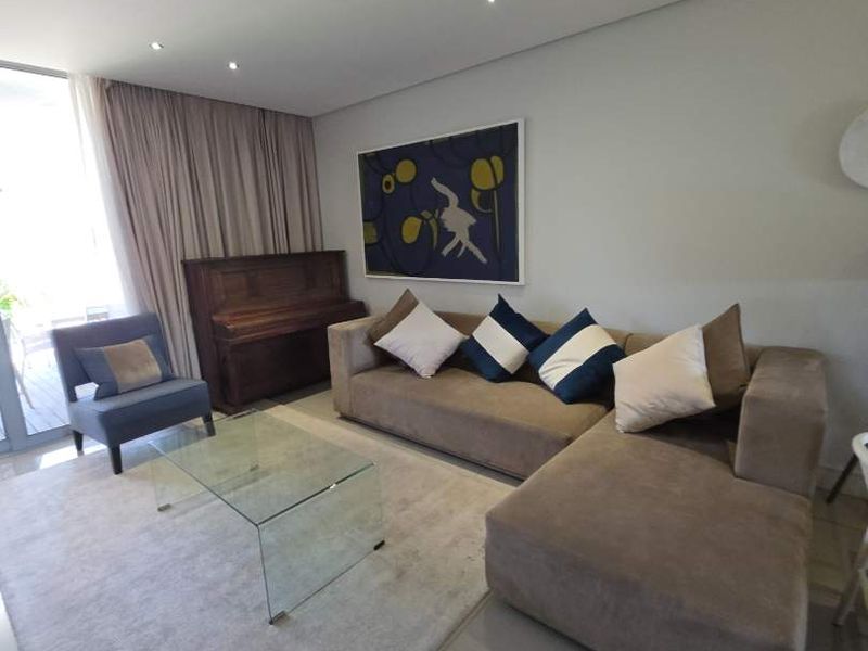 A bright and modern living room featuring large format floor tiles, recessed downlighting, and a sliding glass door providing access to the outdoor area.