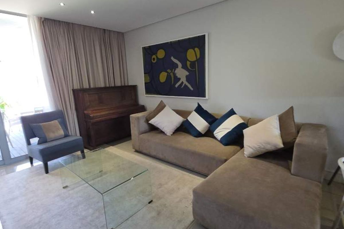 A bright and modern living room featuring large format floor tiles, recessed downlighting, and a sliding glass door providing access to the outdoor area.