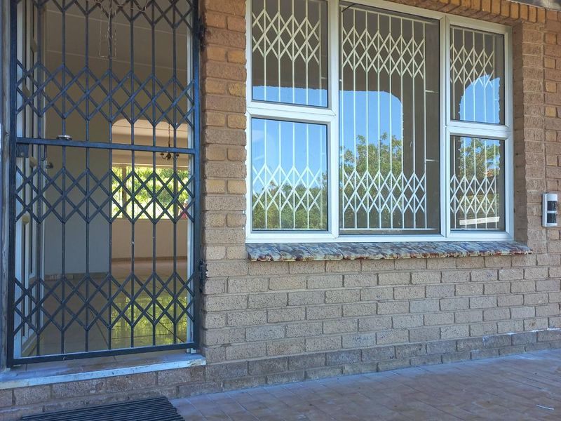 Front entrance area featuring face brick exterior, security gate, and security bars on windows with a tiled patio.