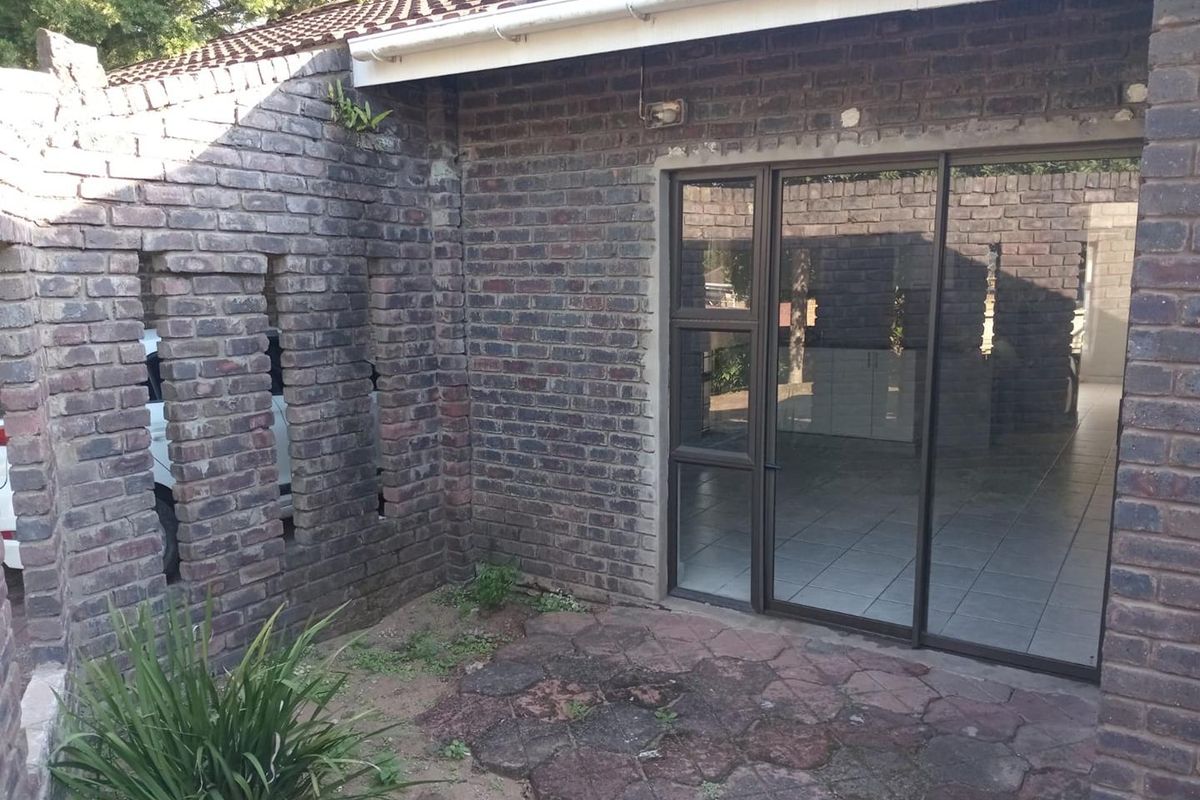 A rear exterior view of the cottage featuring a paved patio area, exposed brick walls, and large sliding glass doors leading into the interior.