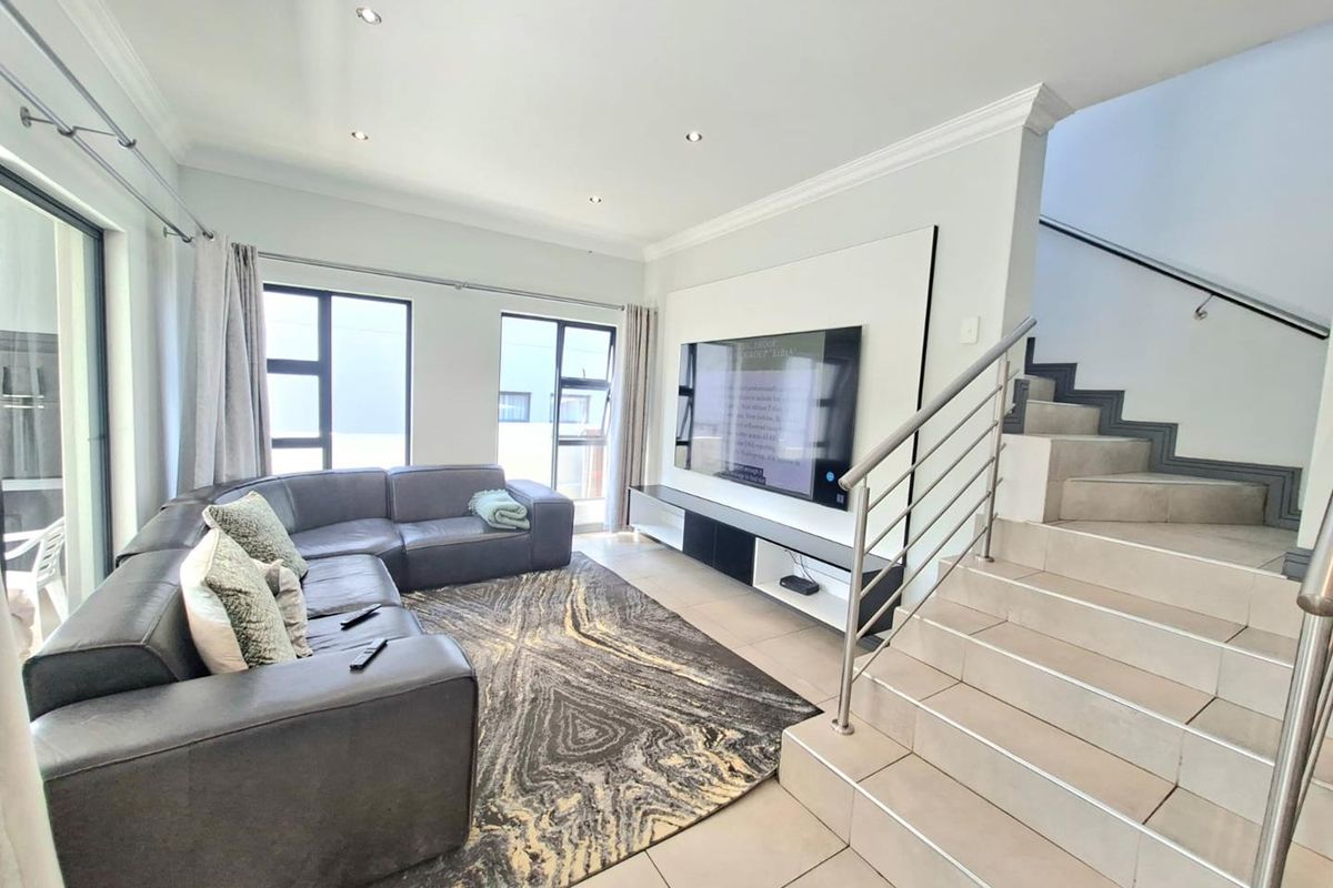 Modern living room featuring tiled floors, a built-in media wall, recessed lighting, and an adjacent staircase with a contemporary stainless steel balustrade.