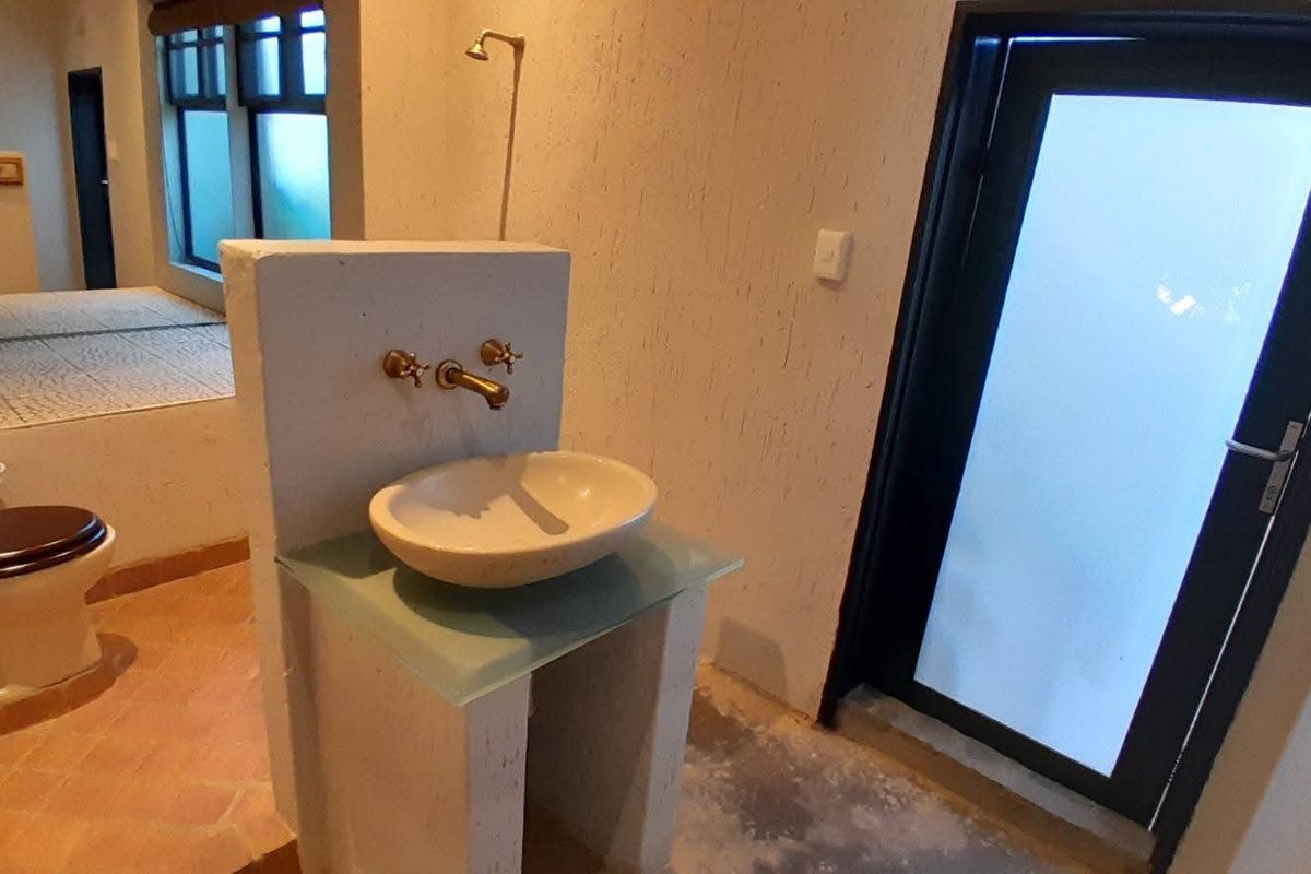 A bathroom featuring a stone vessel sink on a glass vanity, wall-mounted brass taps, and a toilet, with an adjacent glass door.