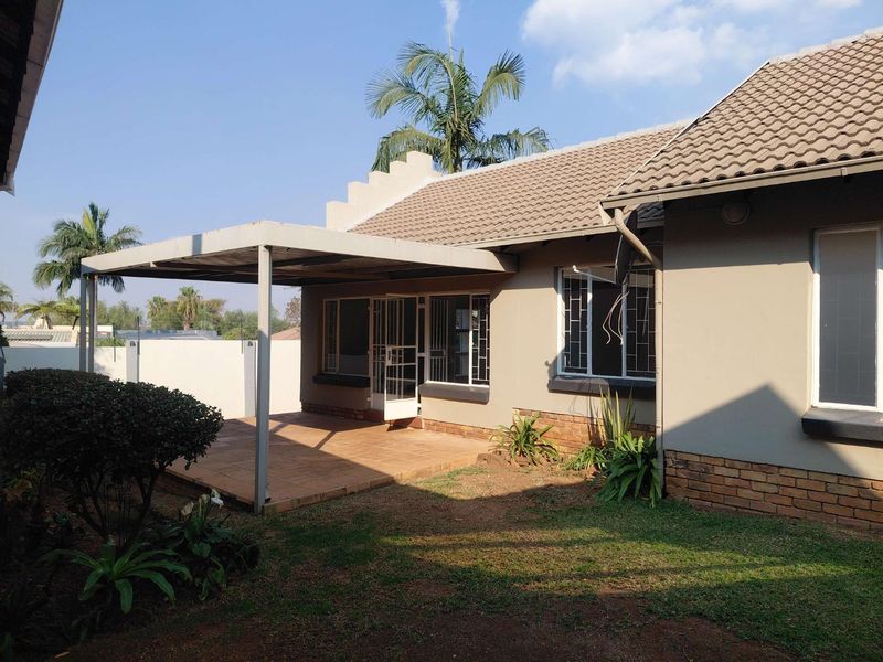 Rear view of the property featuring a covered patio area, tiled roof, and brick base detailing with established garden surroundings.