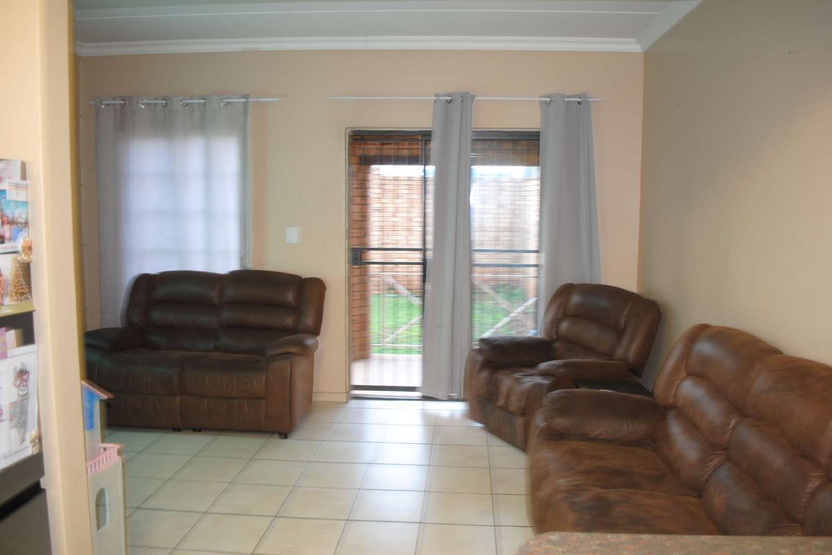A living room featuring tiled flooring, crown molding, and a sliding glass door providing access to the outdoor patio area.