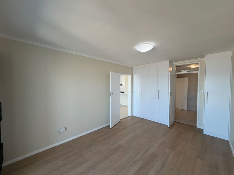 A bright, empty bedroom featuring modern laminate flooring, neutral walls, and ample built-in cupboard storage.