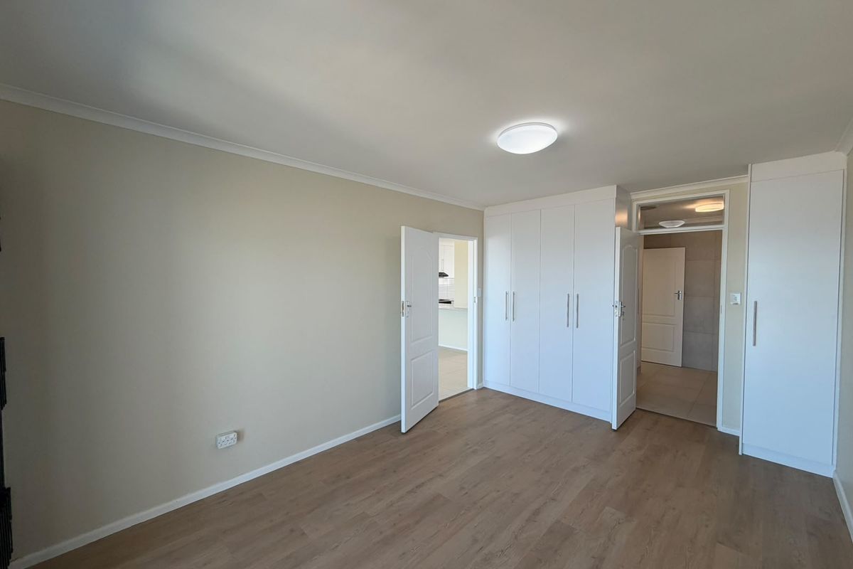 A bright, empty bedroom featuring modern laminate flooring, neutral walls, and ample built-in cupboard storage.