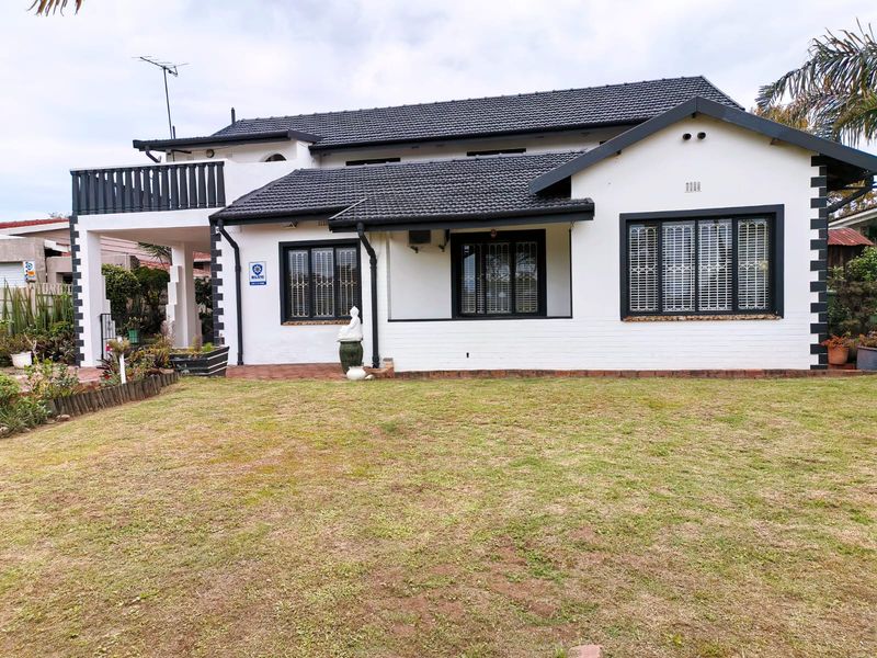 Rear view of a well-maintained house featuring a tiled roof, balcony, and paved patio area overlooking the garden.