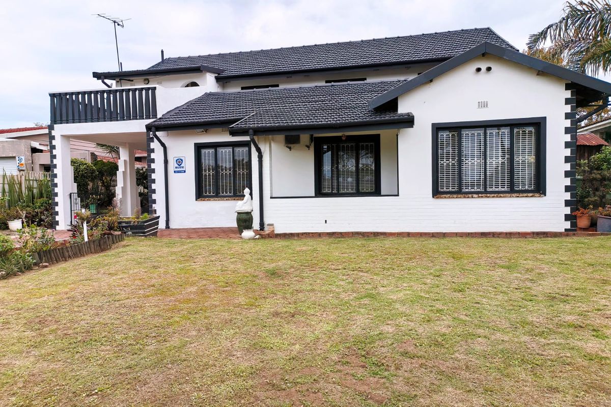 Rear view of a well-maintained house featuring a tiled roof, balcony, and paved patio area overlooking the garden.