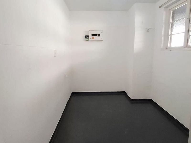 A vacant utility space featuring dark vinyl flooring, a wall-mounted electrical distribution board, and a window with security bars.