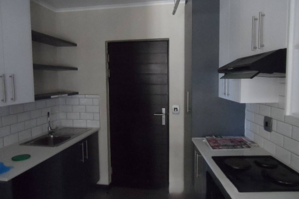 Modern kitchen featuring dark cabinetry, white subway tile backsplash, built-in electric hob with extractor fan, and stainless steel sink.