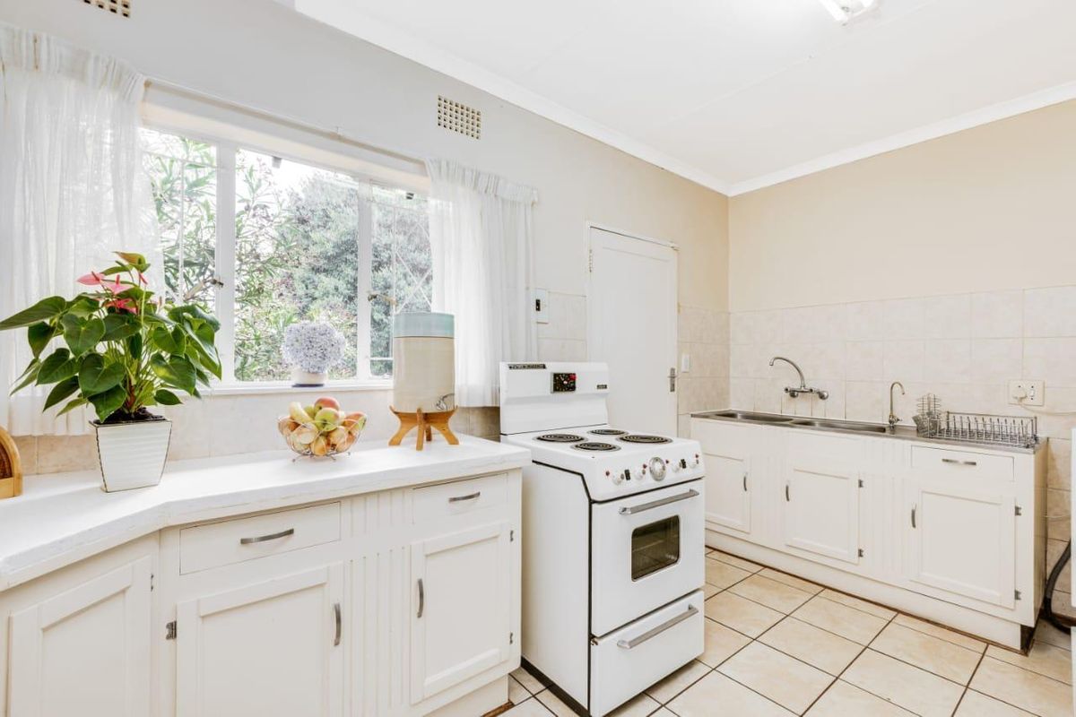 A functional kitchen featuring white cabinetry, tiled flooring, a built-in sink, and a freestanding electric stove.