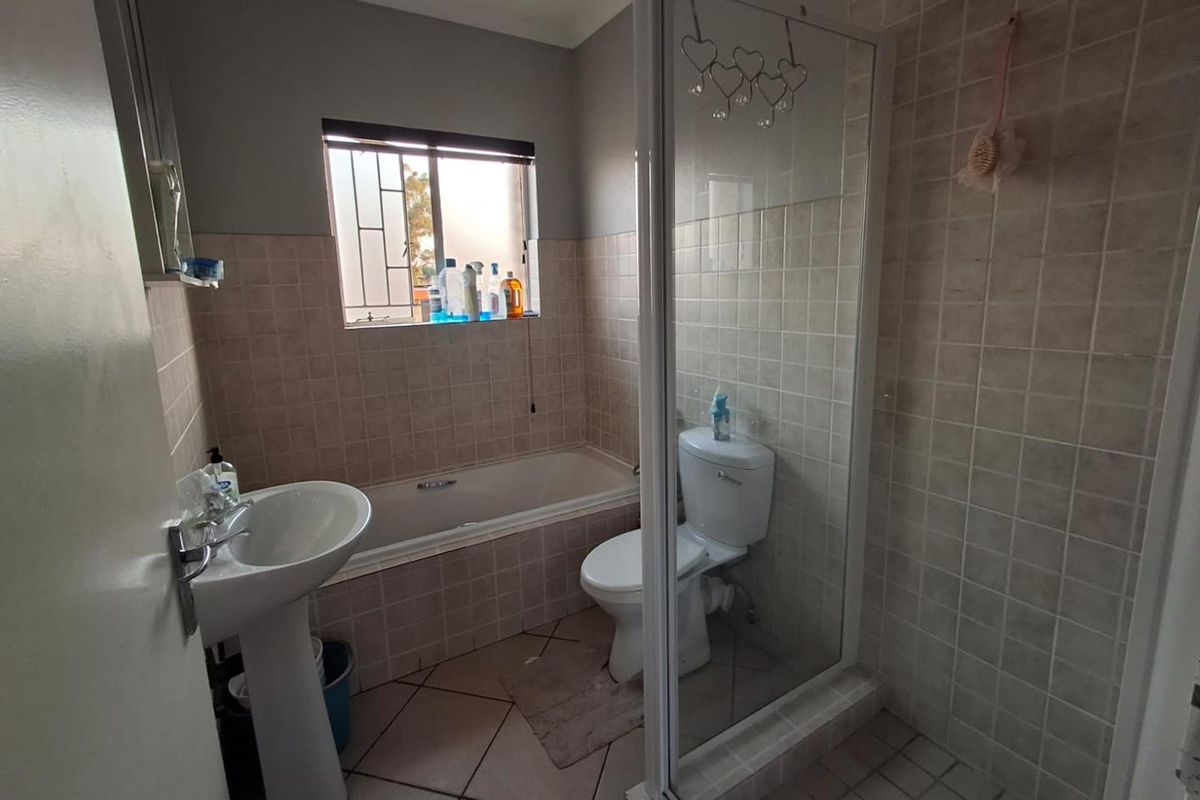 A functional bathroom featuring a pedestal basin, a built-in bathtub, and a separate glass-enclosed shower with tiled finishes throughout.