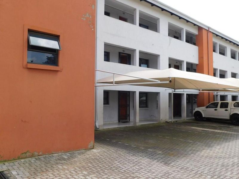 Exterior view of a multi-level townhouse complex featuring a paved driveway and covered parking bays.