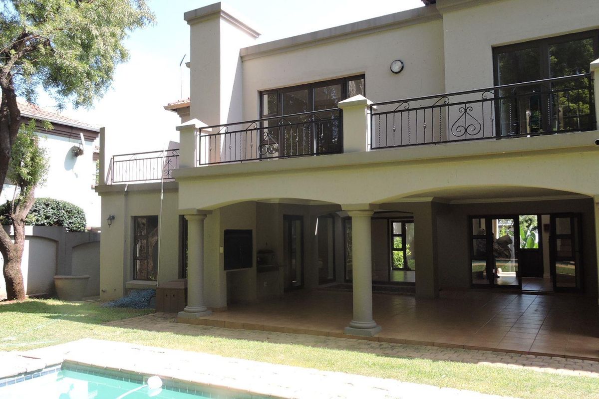 Rear view of the property featuring a covered patio with built-in braai, an upper-level balcony with wrought iron railings, and a swimming pool.