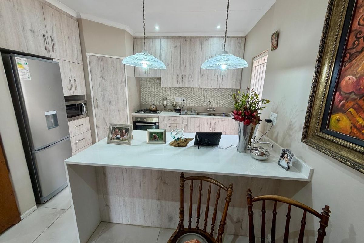 Modern kitchen featuring light wood-grain cabinetry, stone countertops, a breakfast bar, and integrated appliances with a stylish tiled backsplash.