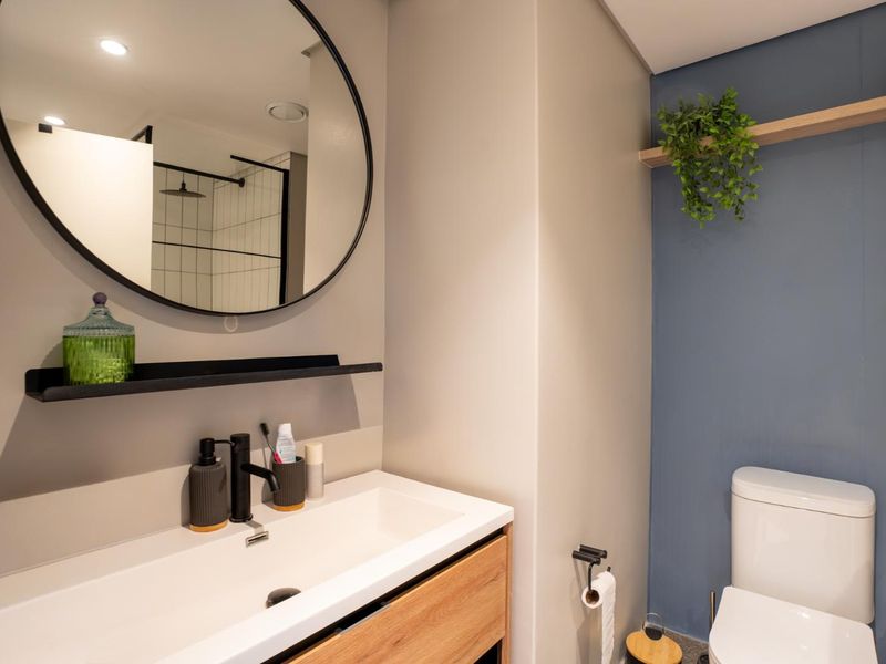 Modern bathroom featuring a sleek vanity with integrated basin, black fixtures, a round mirror, and a separate shower enclosure with a glass screen.