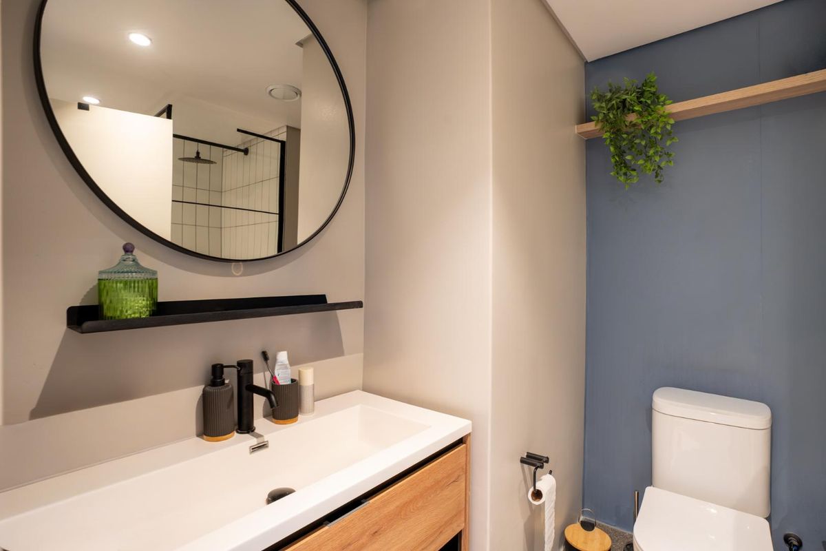 Modern bathroom featuring a sleek vanity with integrated basin, black fixtures, a round mirror, and a separate shower enclosure with a glass screen.