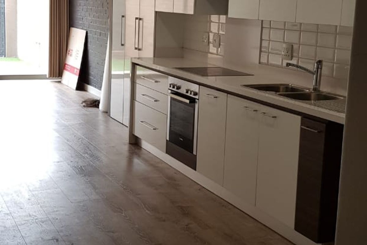 Modern kitchen featuring sleek white cabinetry, integrated appliances, a tiled backsplash, and an exposed brick wall, leading to an outdoor patio area.