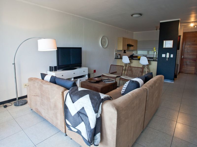 Open-plan living area featuring tiled flooring and a compact kitchen with a breakfast bar, creating a functional and connected living space.