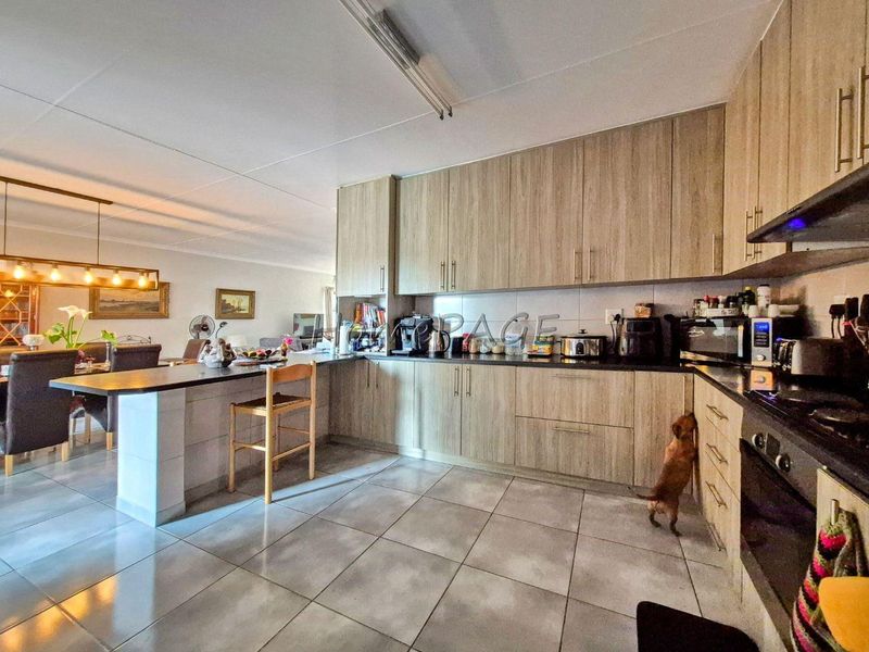 Open plan kitchen and dining area featuring wood-look cabinetry, a breakfast bar, tiled flooring, and integrated cooking appliances.